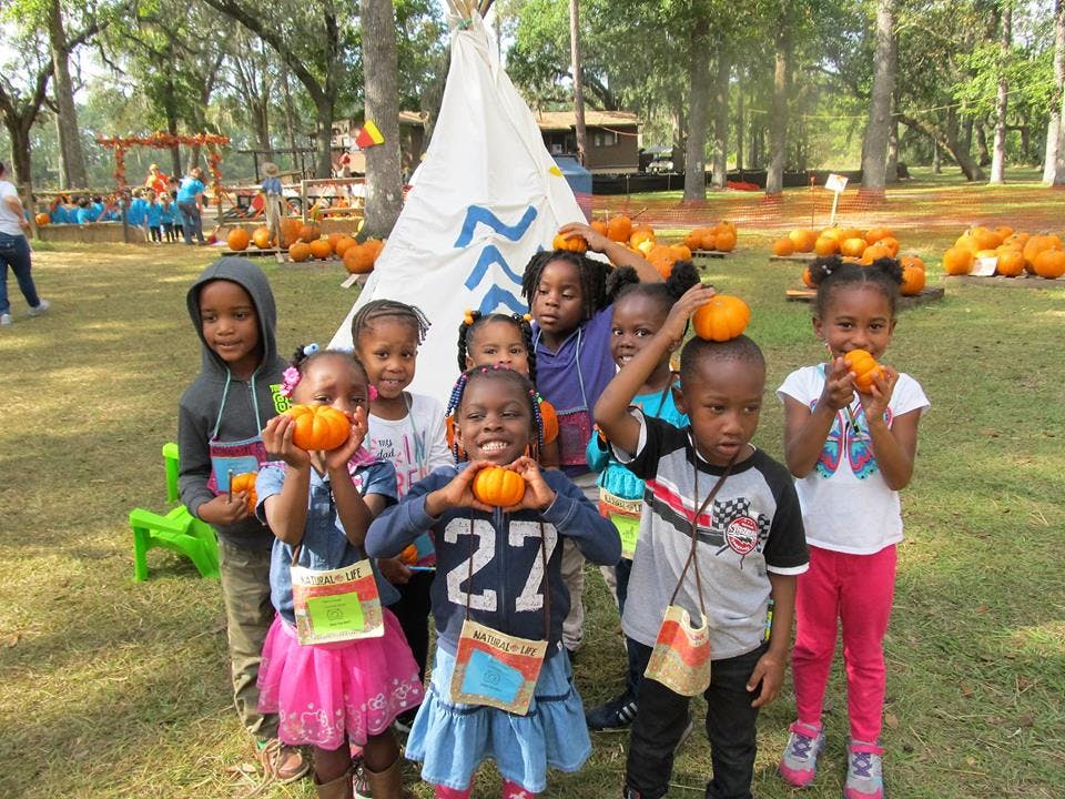 Group of children holding small pumpkins in front of a teepee
