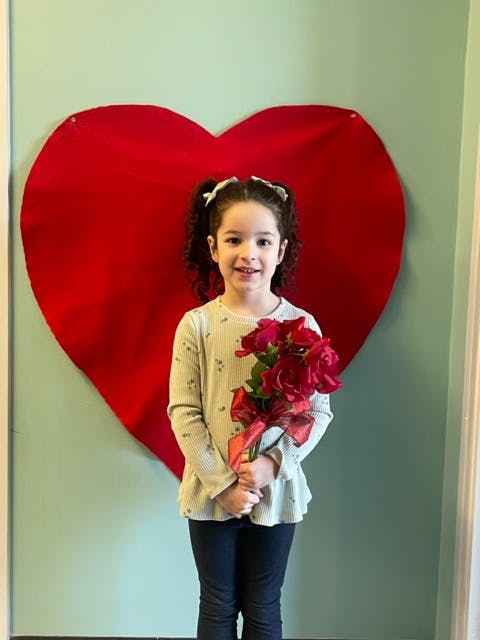 Child holding a bouquet of red roses in front of a large red heart
