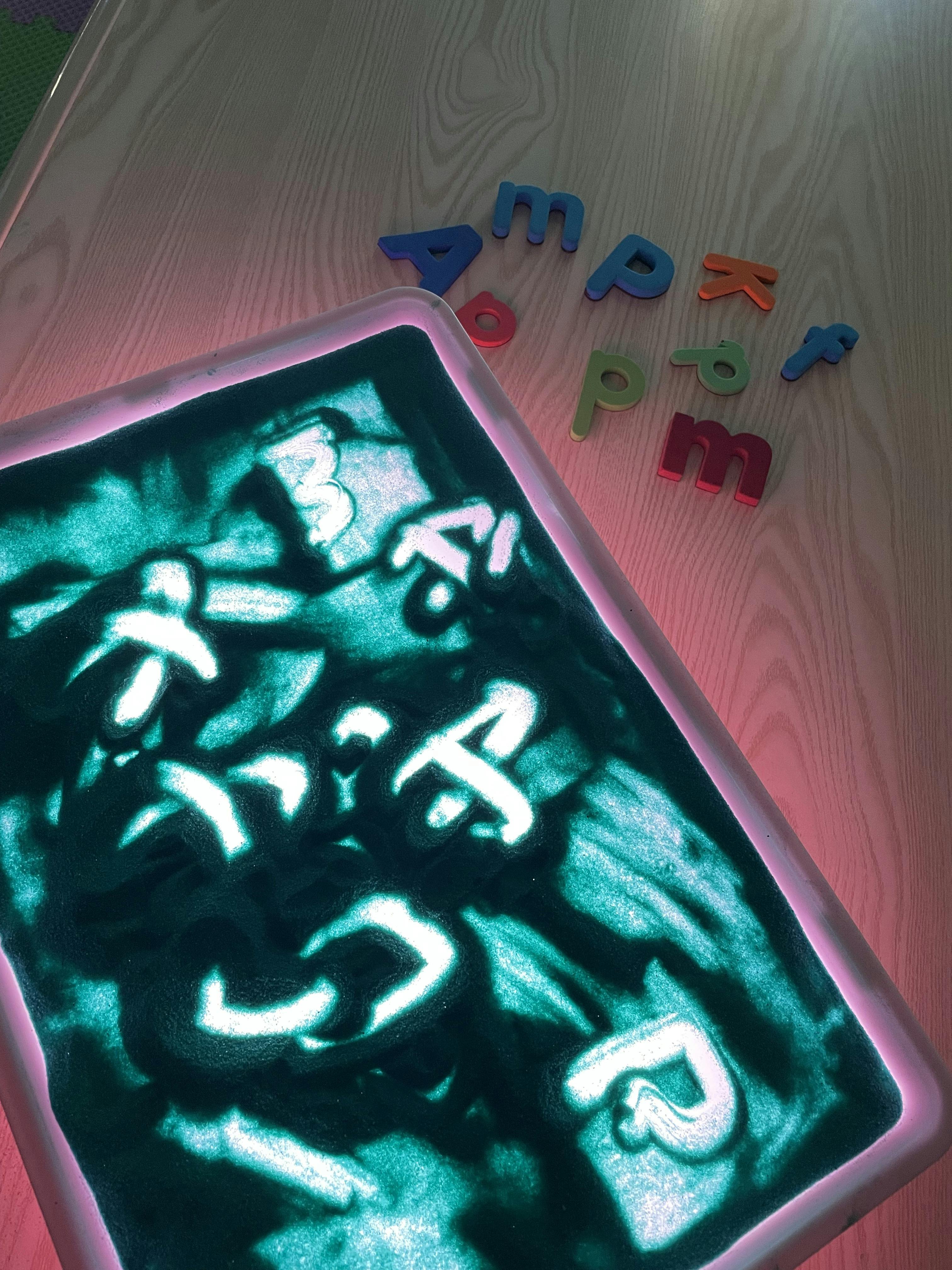 Lighted sand tray with writing and magnetic letters on a table