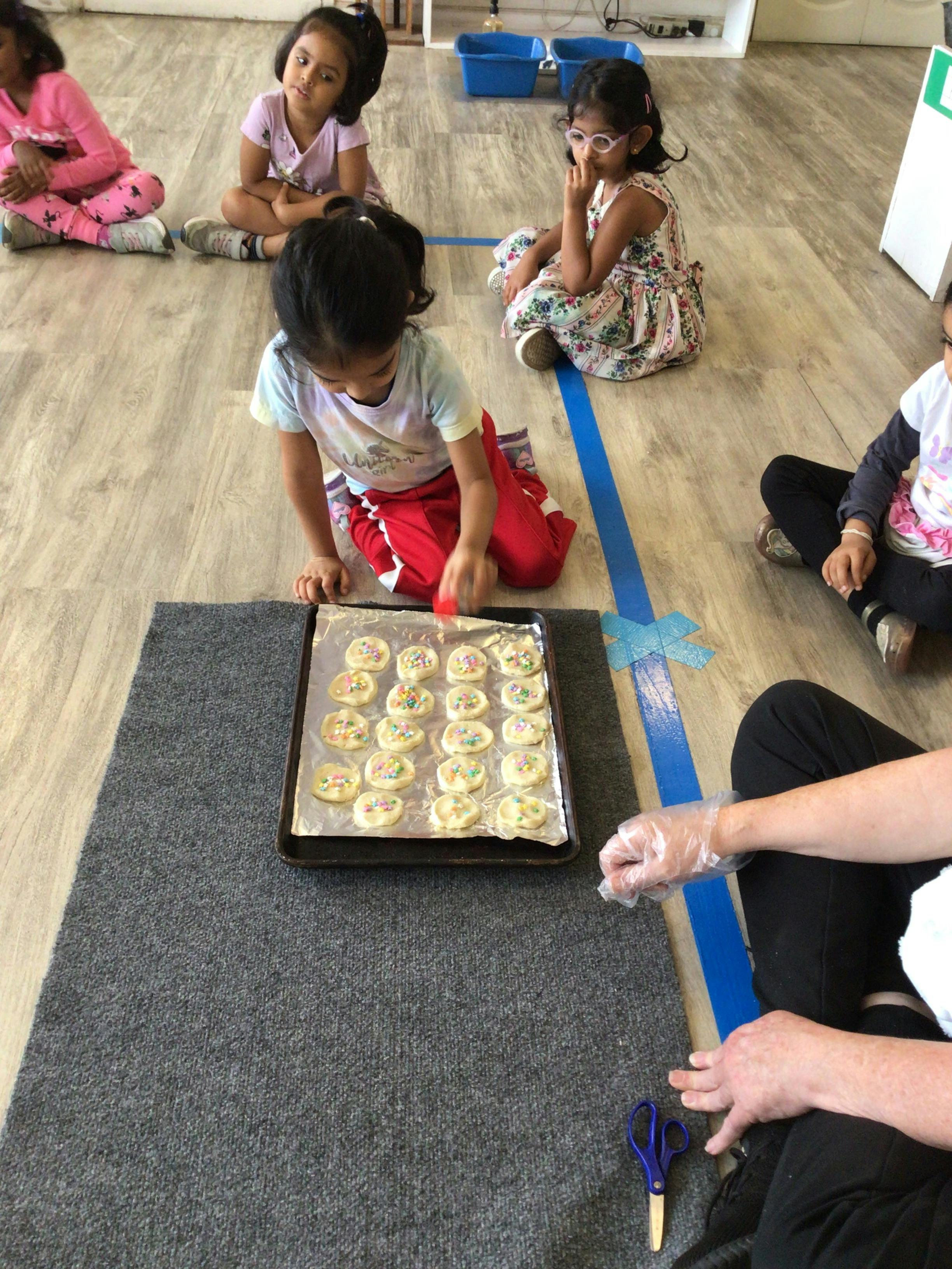 A child placing sprinkles on dough rounds on a baking sheet
