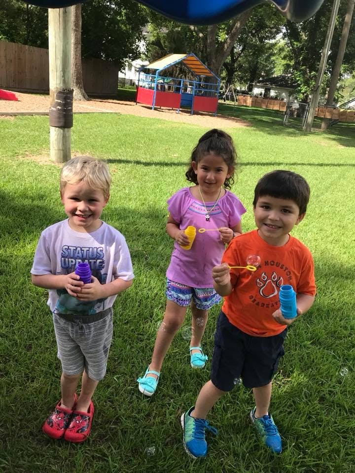 Three children holding bubble wands and bottles on grass