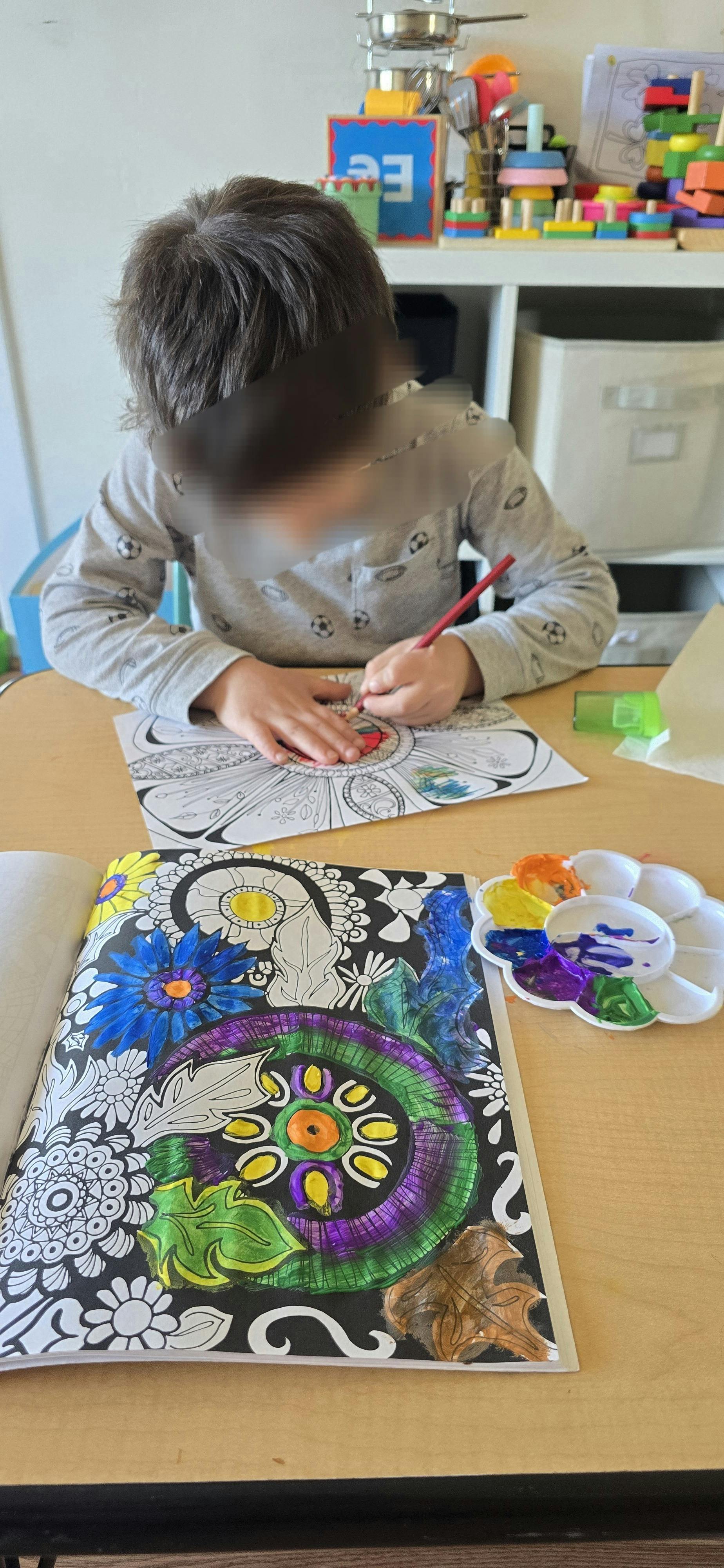 Child coloring in a coloring book at a table with paints nearby