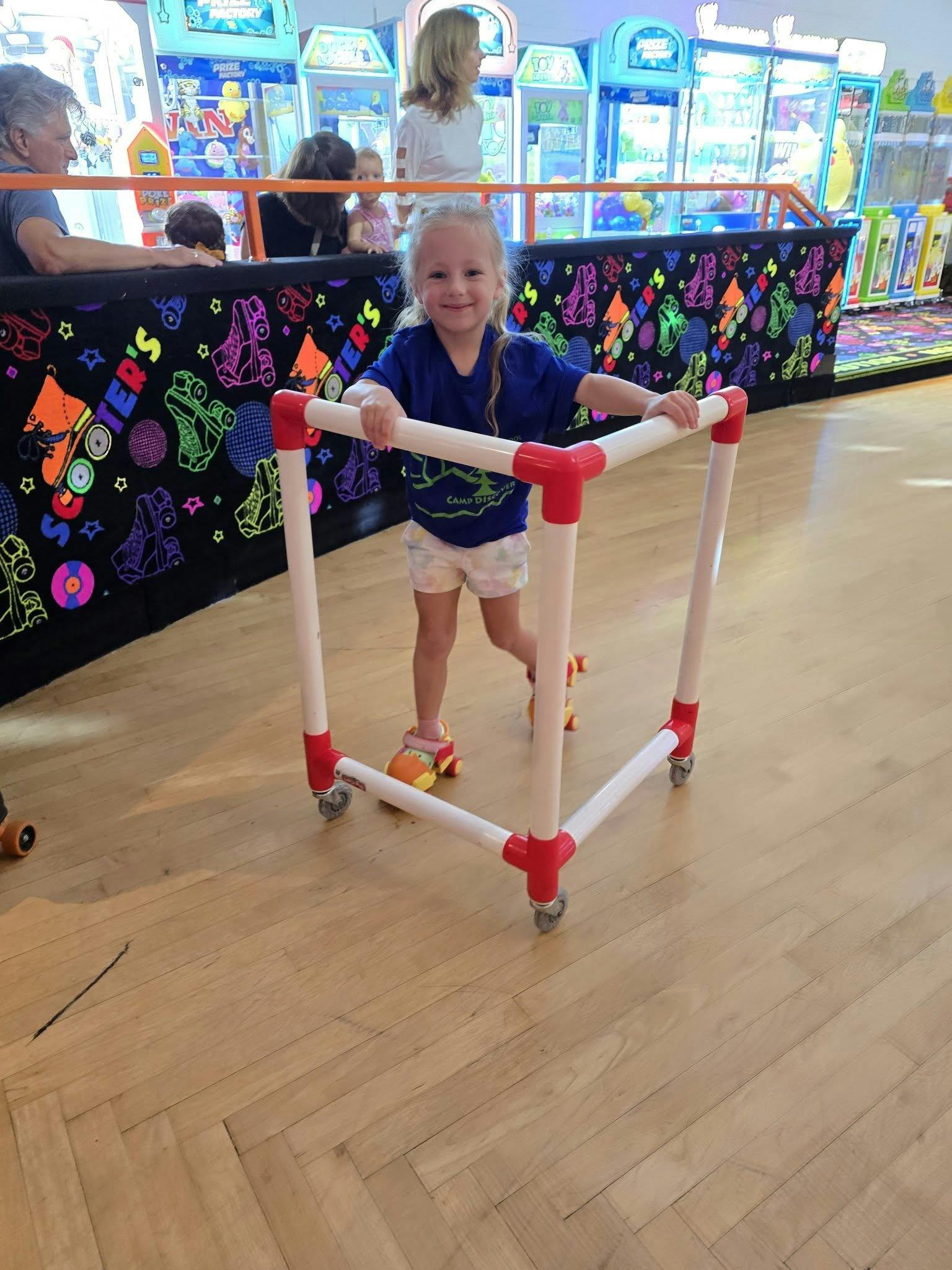 Child on roller skates holding a red and white walker at a roller rink