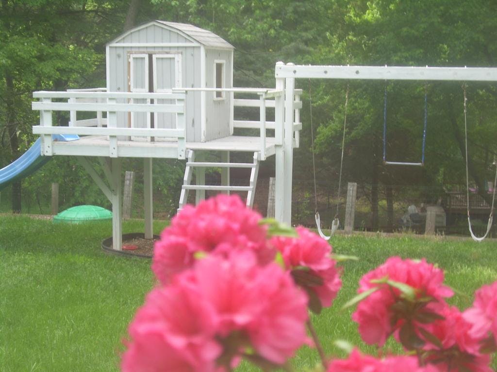 Playhouse with slide and swing set in a grassy yard, with pink flowers in foreground