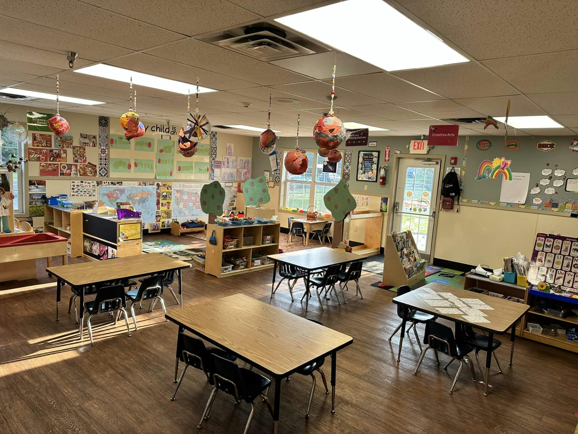 Empty classroom with student tables and chairs, decorated walls, and craft supplies