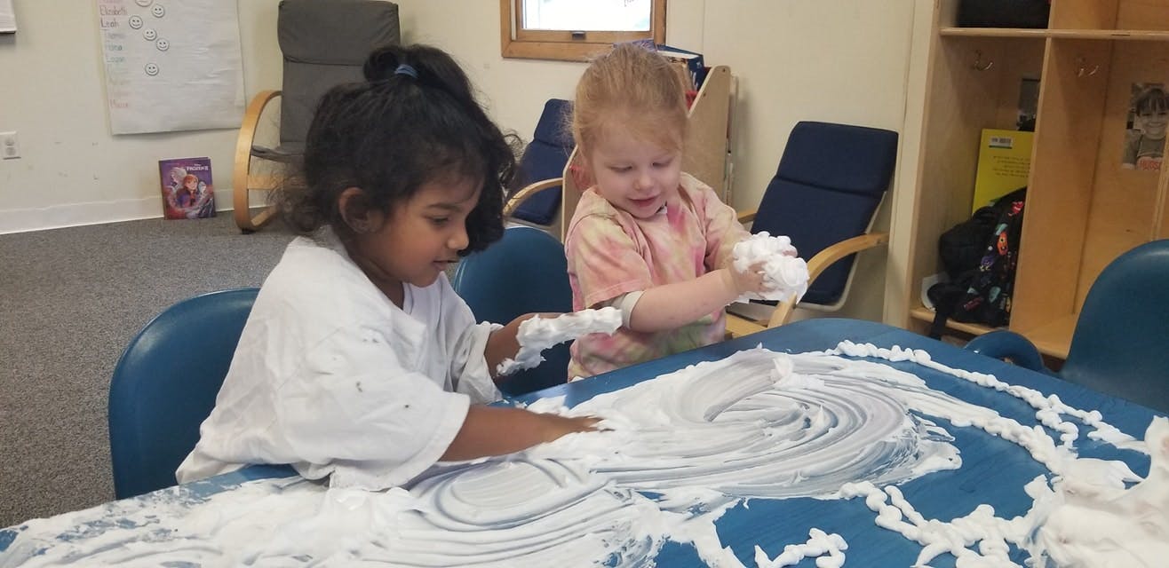 Two children playing with shaving cream on a table