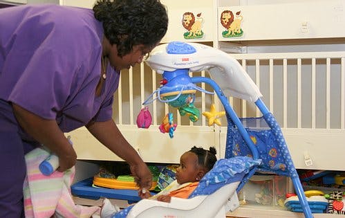 Person leaning over to interact with a child in a baby swing