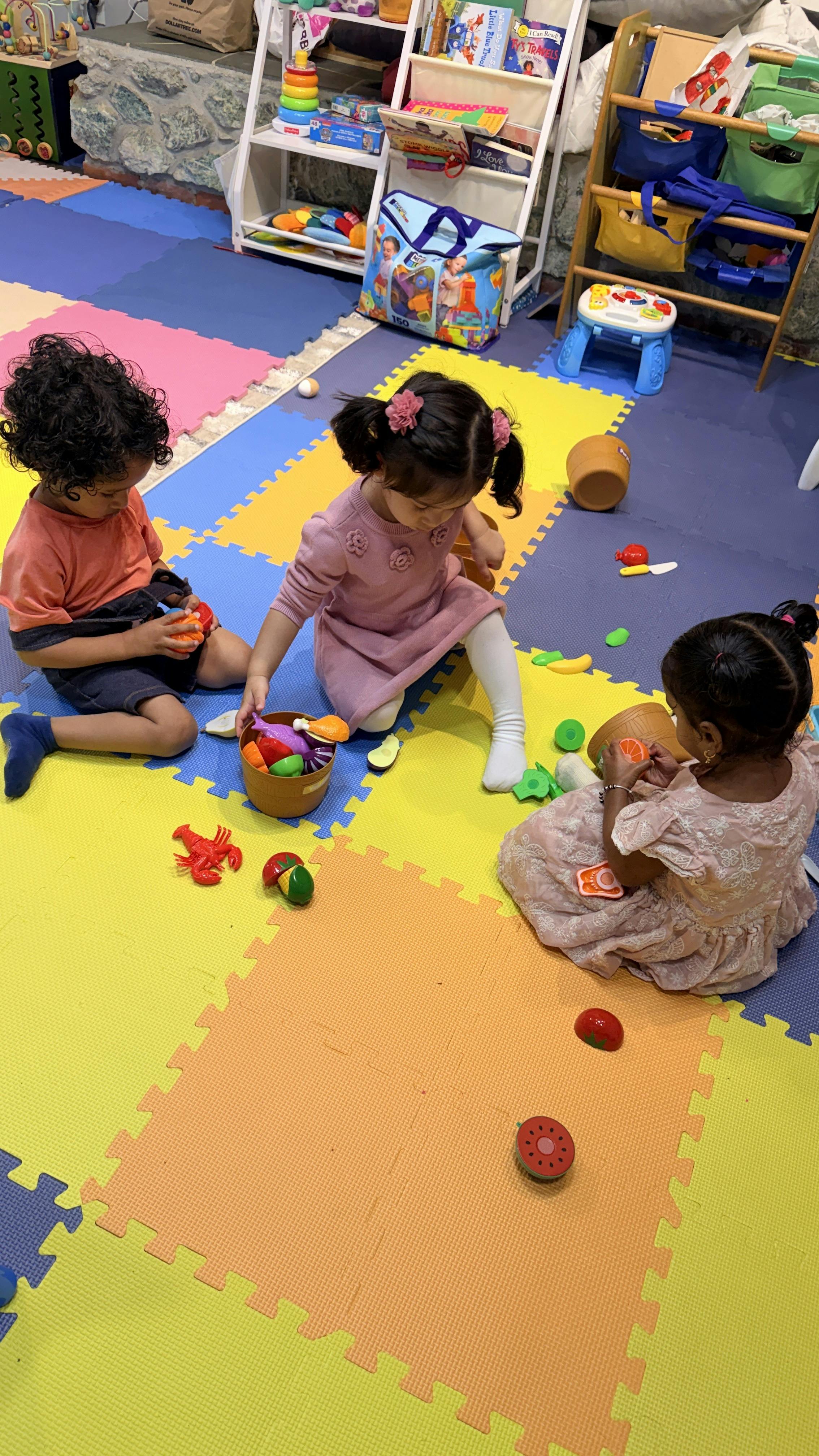 Three children playing with toy food on a colorful foam floor mat