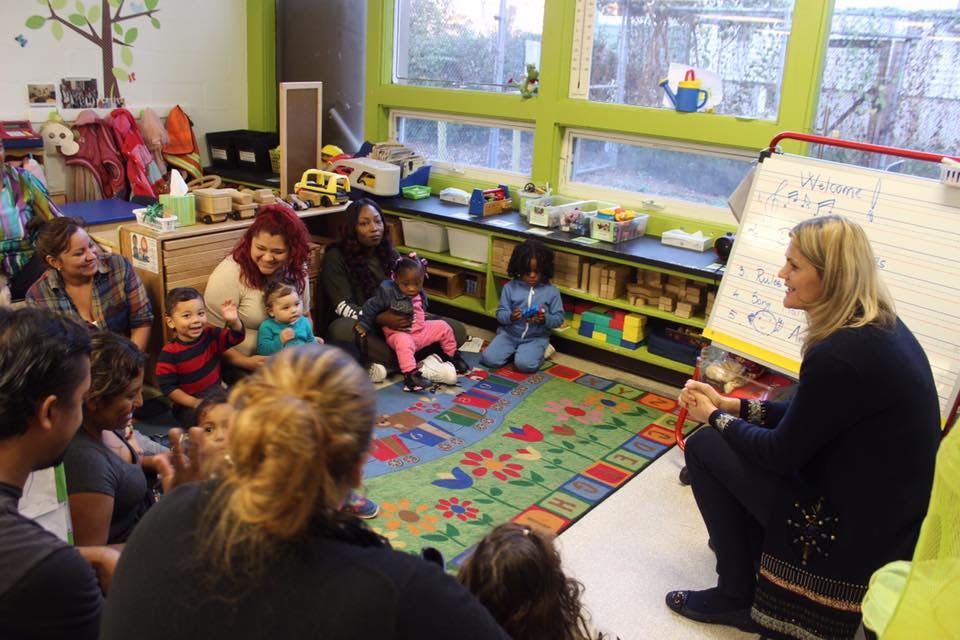 People and children sitting on a rug in a classroom listening to a person