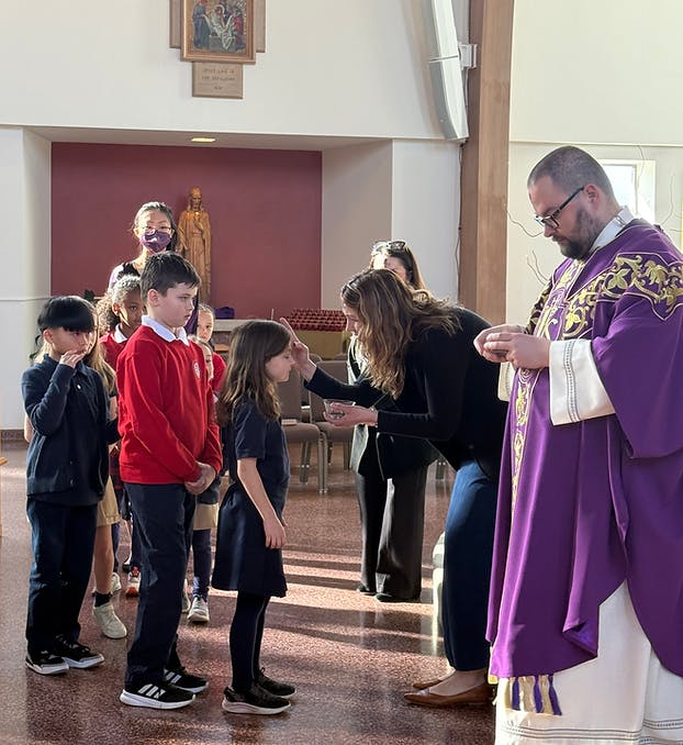 Adult applying ashes to a child's forehead, other children watching