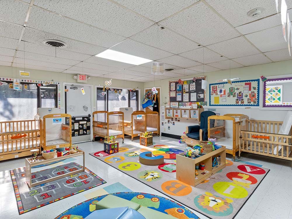Baby room with several cribs, colorful playmats, and toys