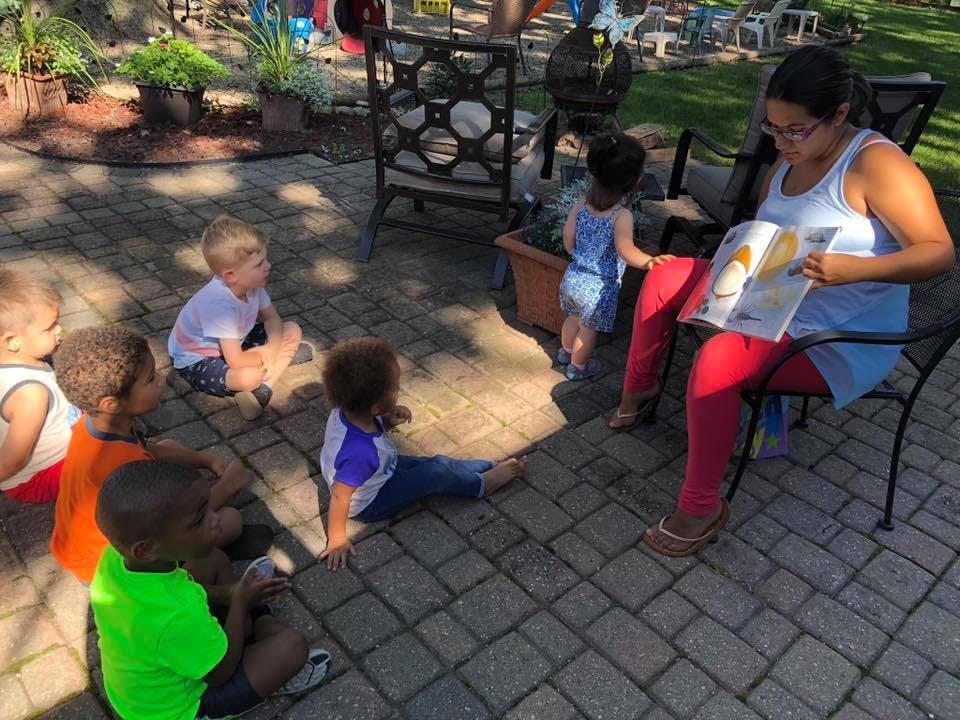 Person reading a book to several children sitting on the ground