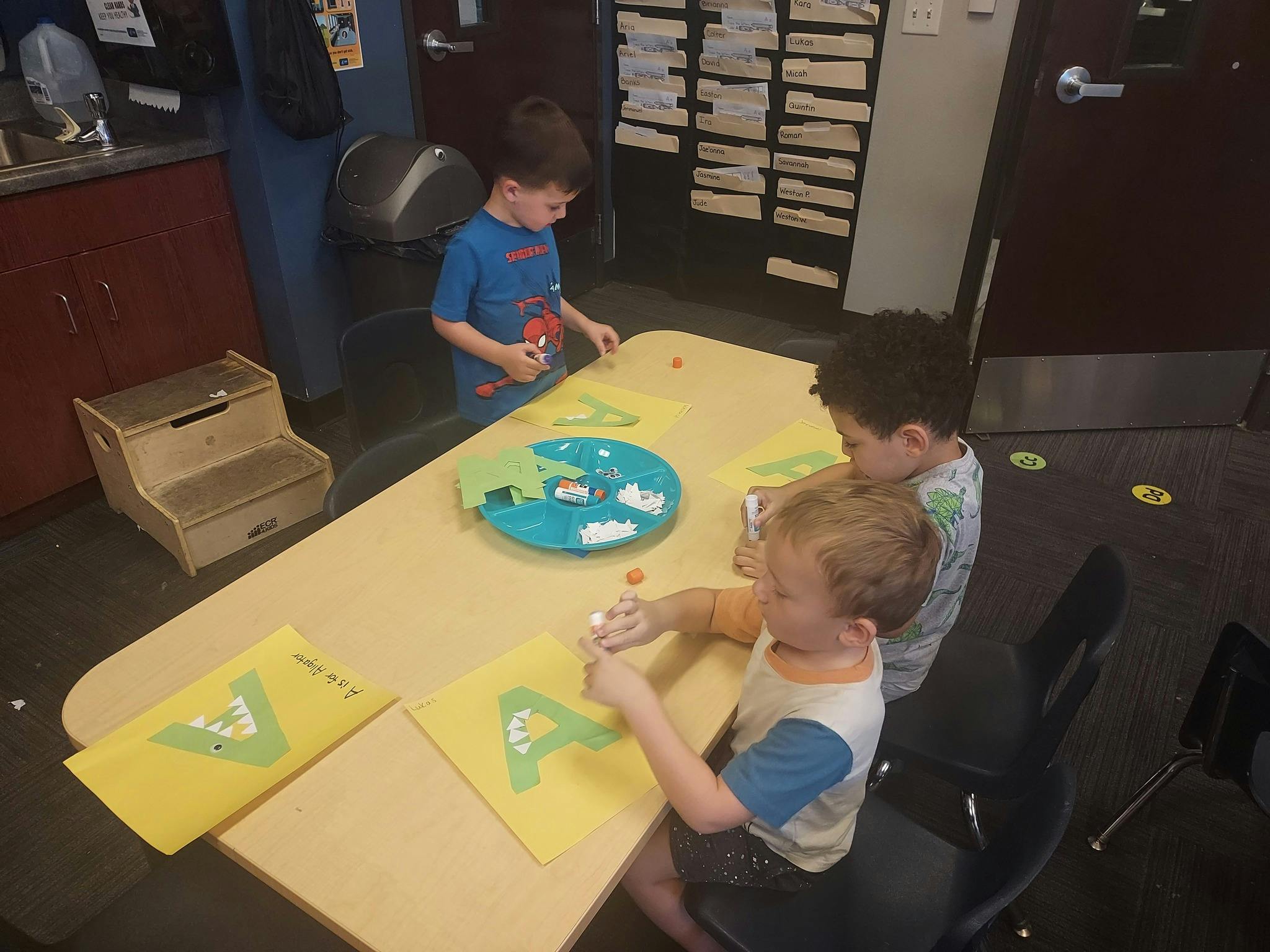 Three children doing crafts at a table in a classroom