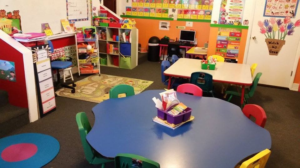 Classroom with small tables and chairs, shelves with toys and books