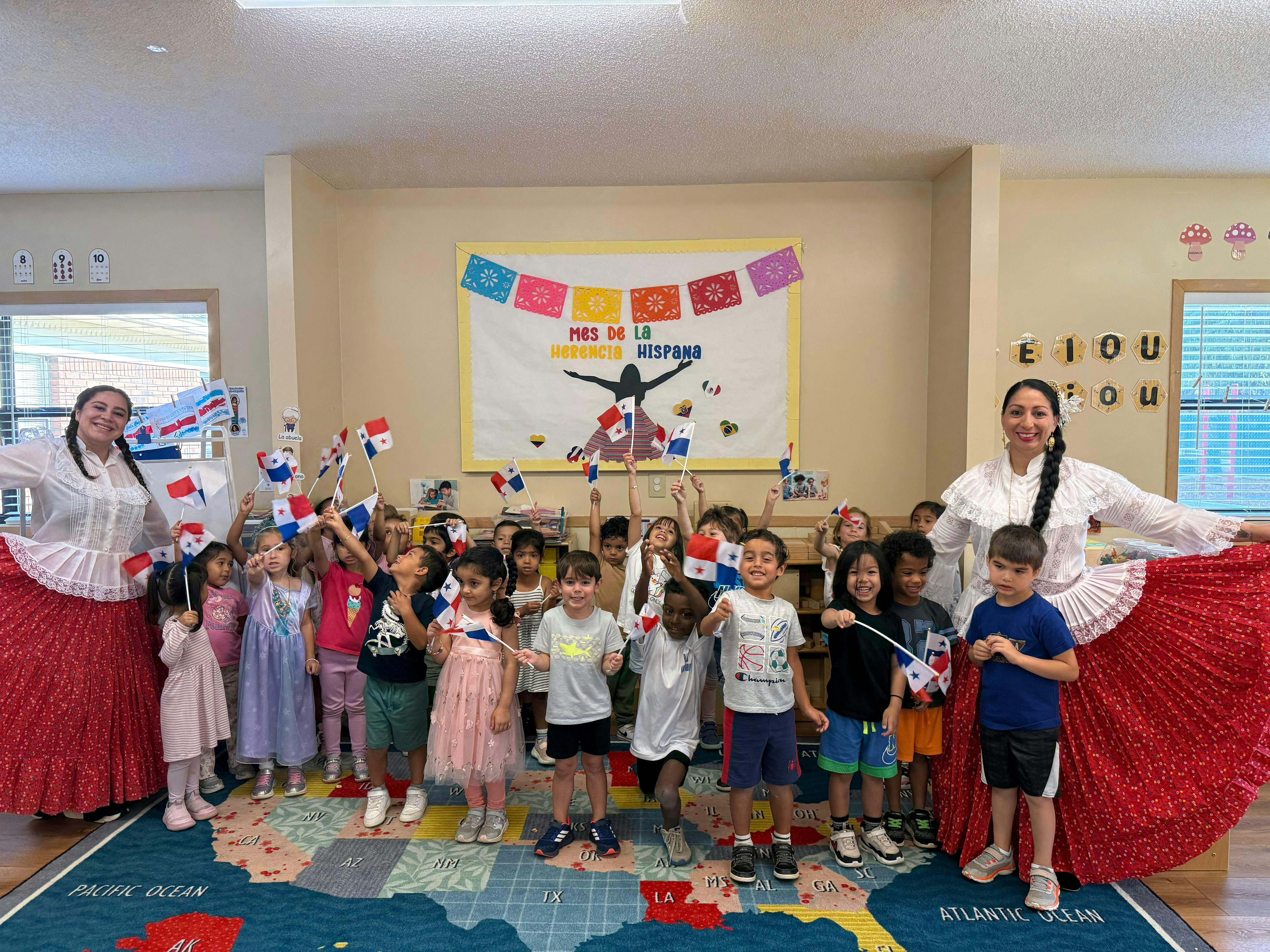 Two people in traditional dress with a group of children holding flags