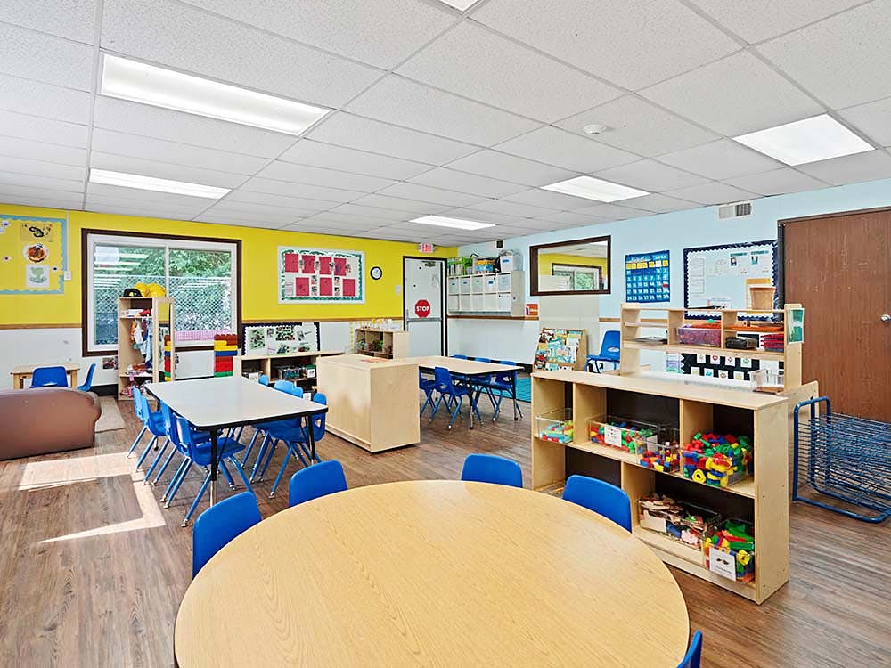 Classroom with child-sized tables and chairs, shelves with toys, and posters on walls