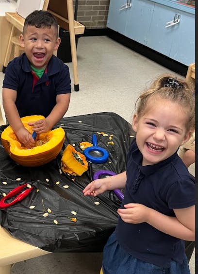 Two children carving a pumpkin in a classroom