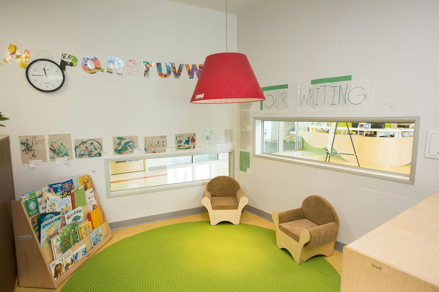 Classroom with a green rug, two small chairs, and a book display