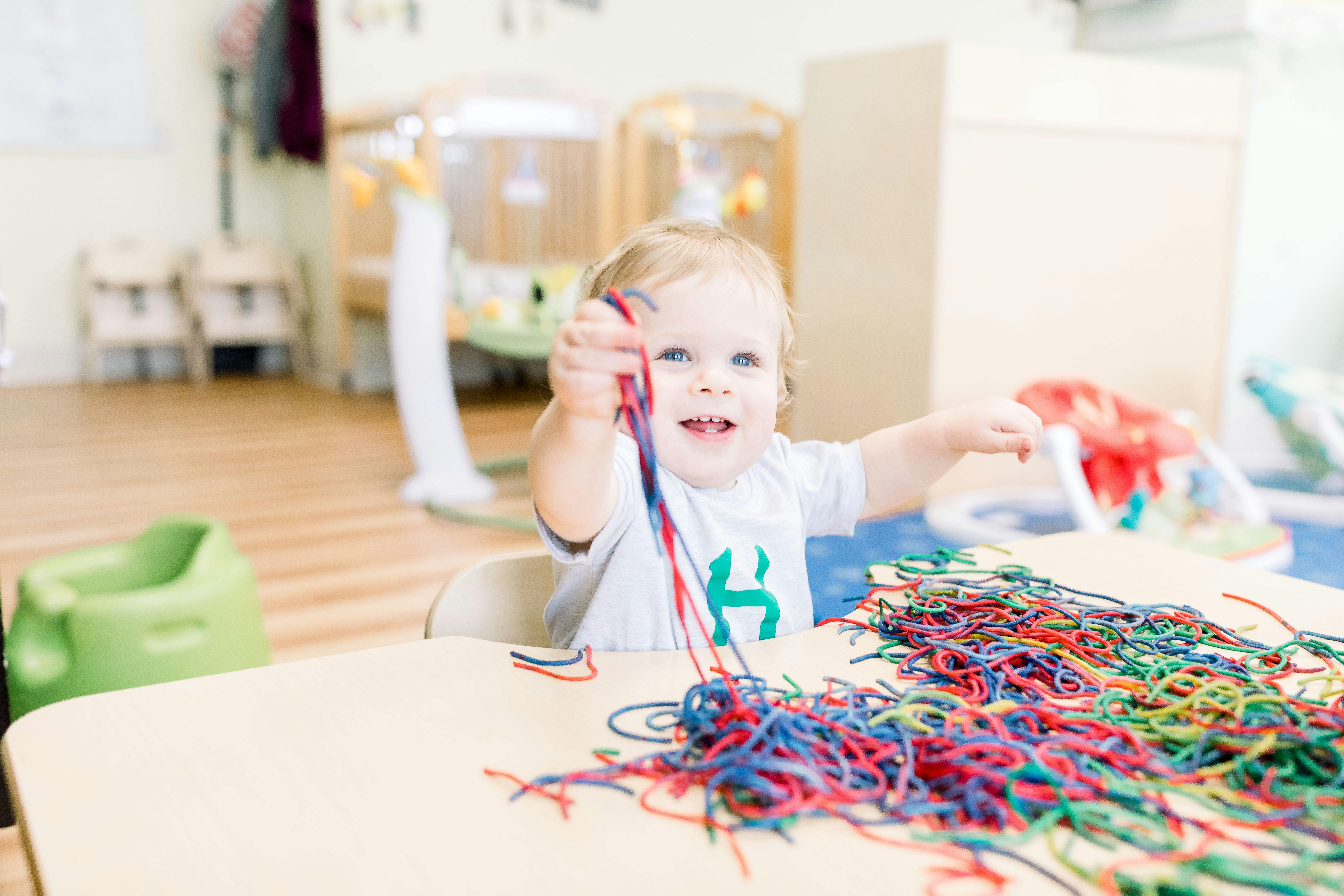 Child playing with colorful laces at a table in a bright room