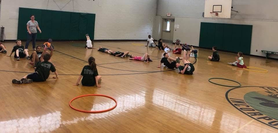 Children and an adult sitting on a gymnasium floor