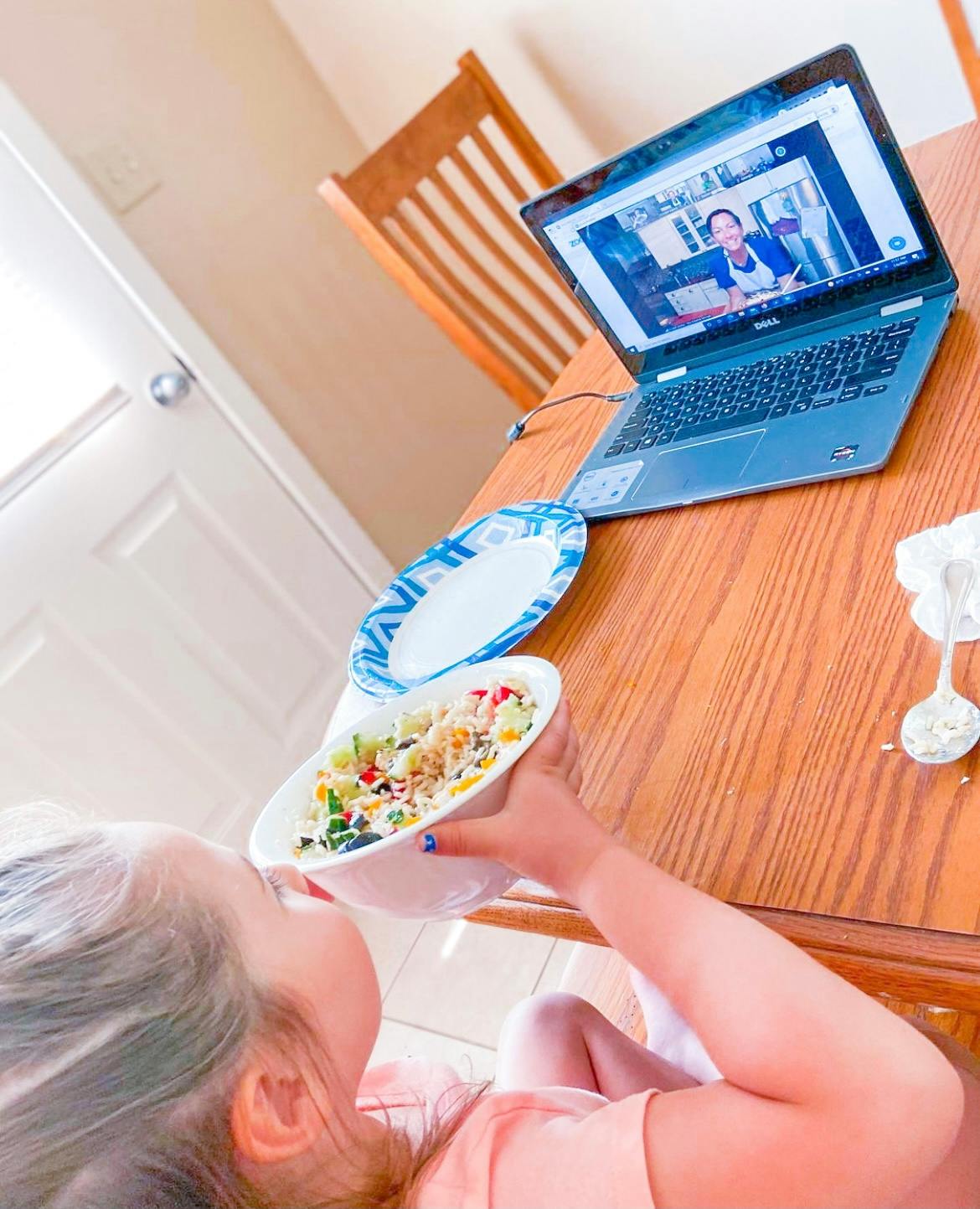 Child eating from a bowl while watching a video on a laptop
