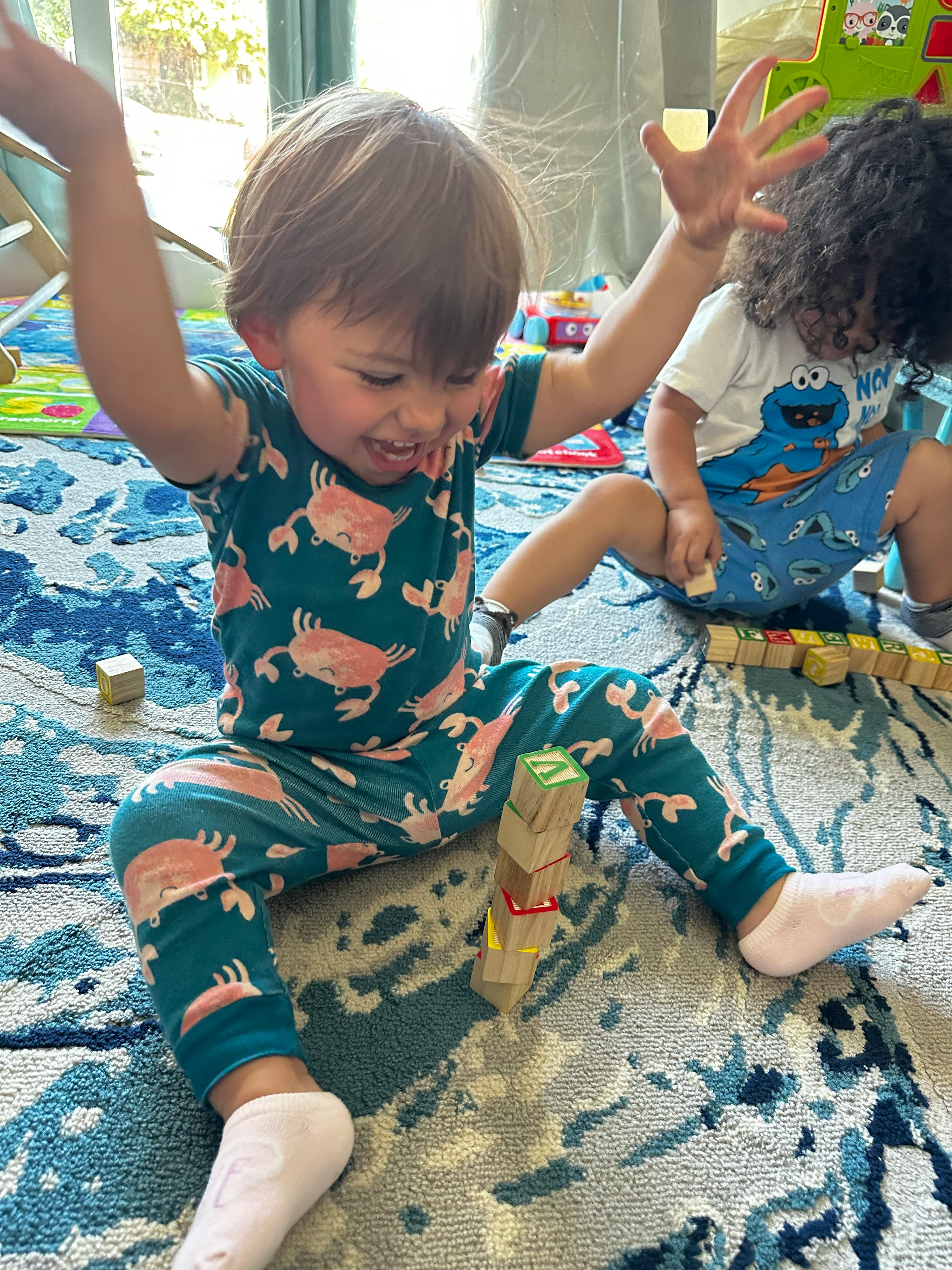 Child in crab pajamas playing with blocks on a rug