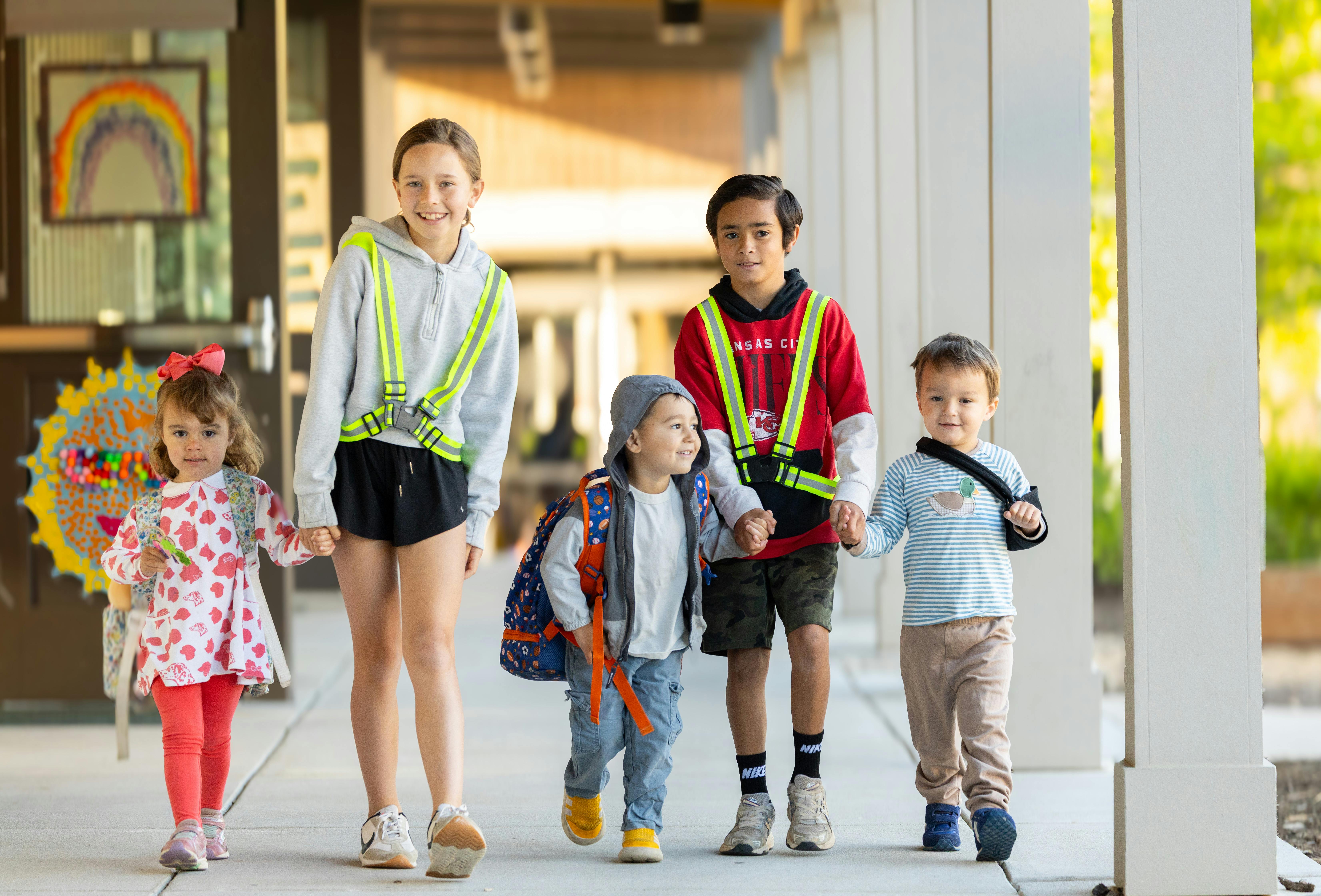 Group of children holding hands while walking in an outdoor corridor