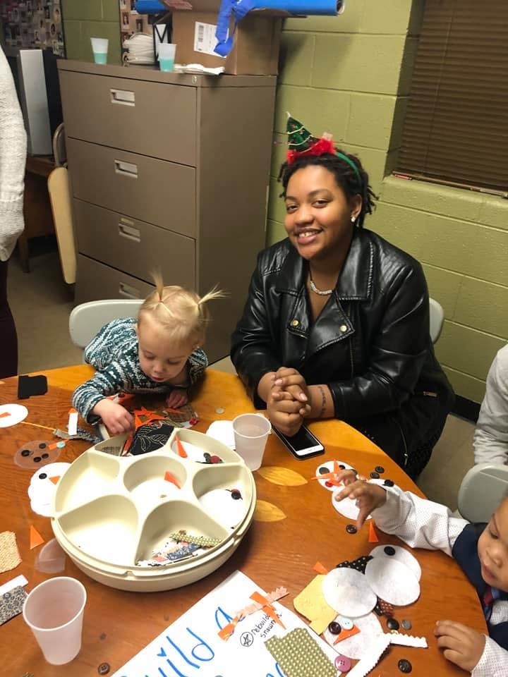 Person in a party hat smiling at a table with a child doing crafts