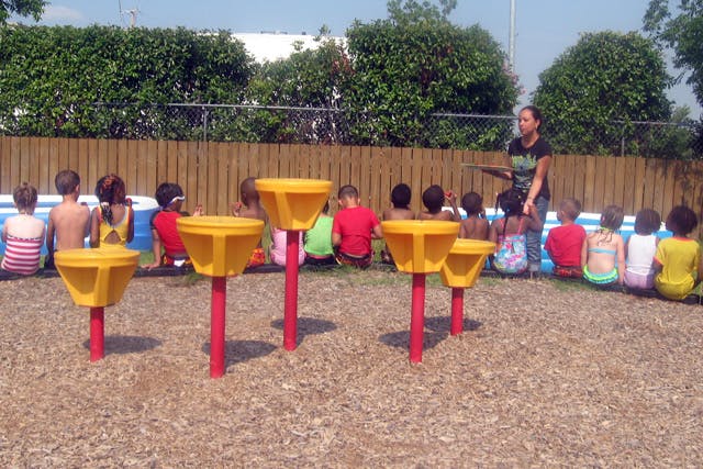 Adult speaking to a group of children sitting on the ground outdoors