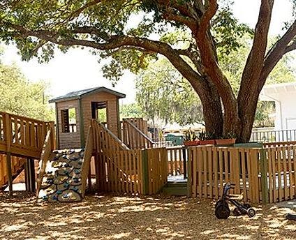 Outdoor playground with wooden structures, fence, and large tree