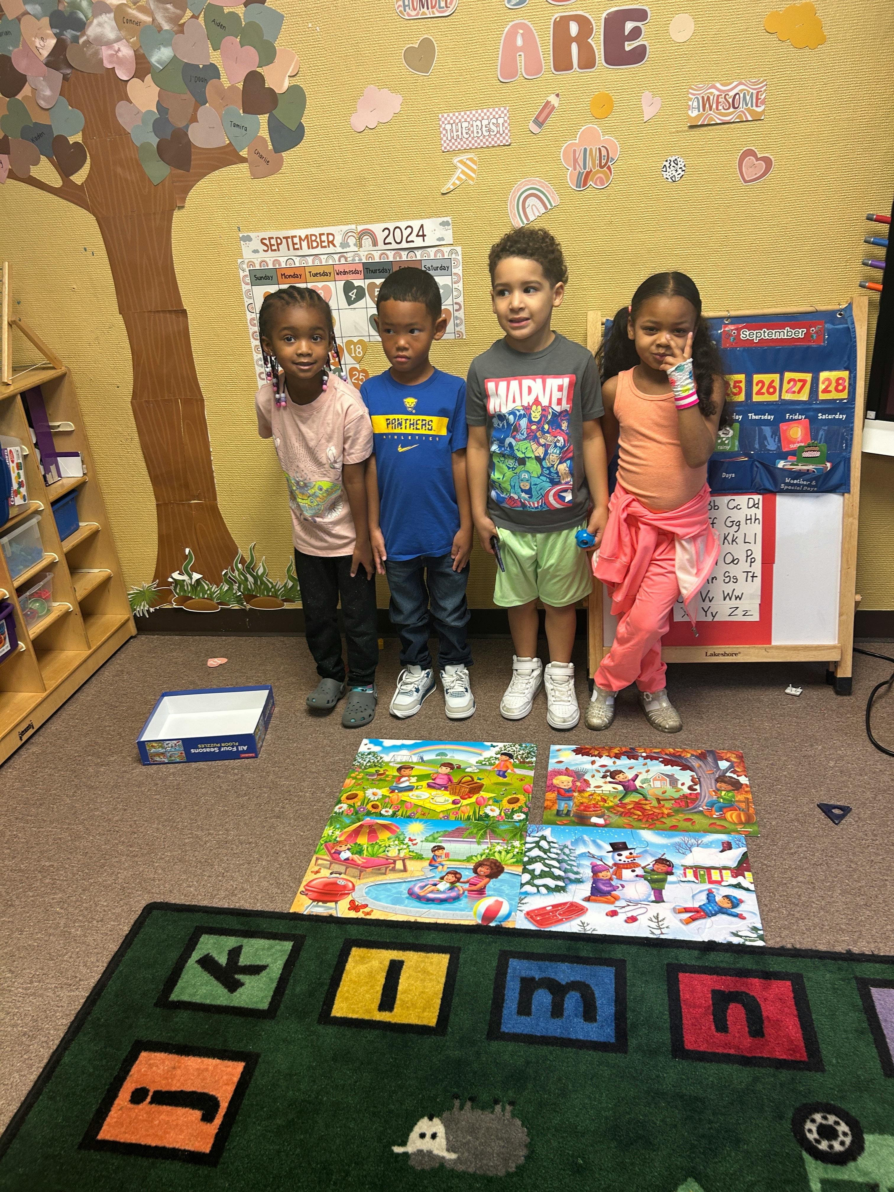 Four children standing in a classroom with puzzles on the floor