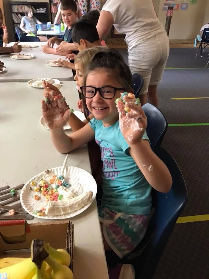 Child with glasses holding up hands covered in frosting and cereal
