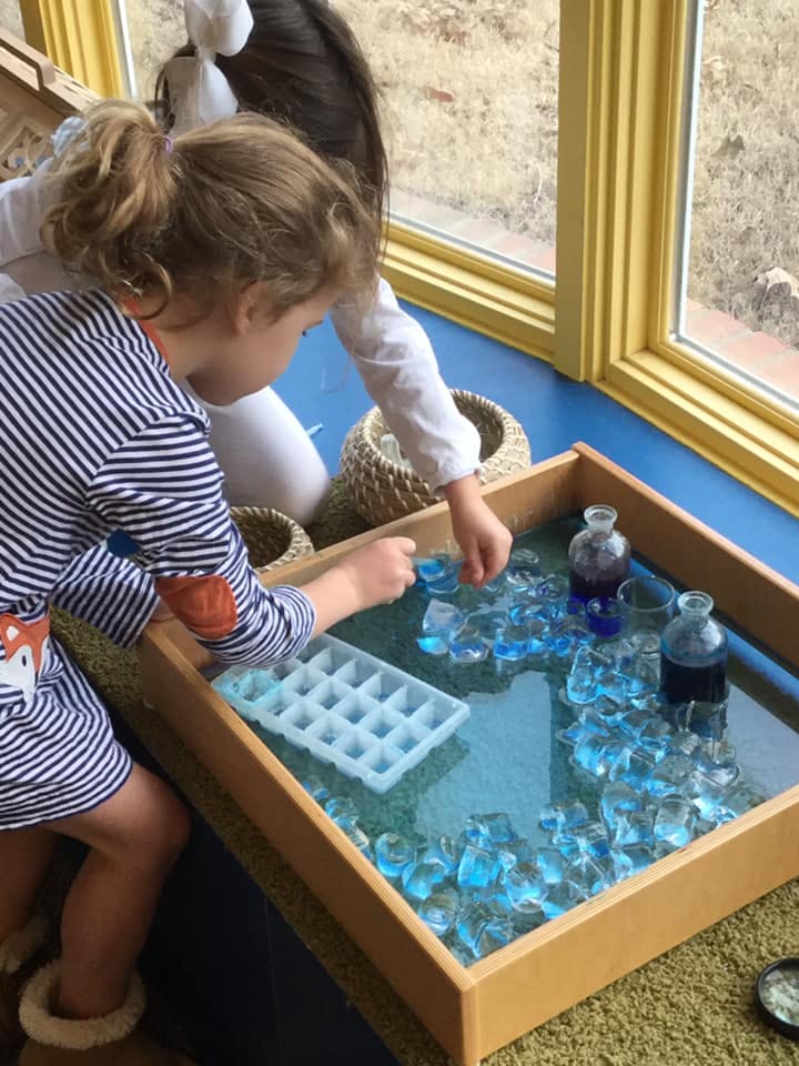 Two children playing with blue glass gems and bottles in a sensory bin