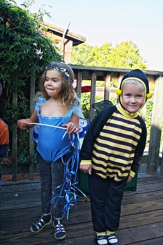 Child in blue costume holding ribbons next to child in bee costume