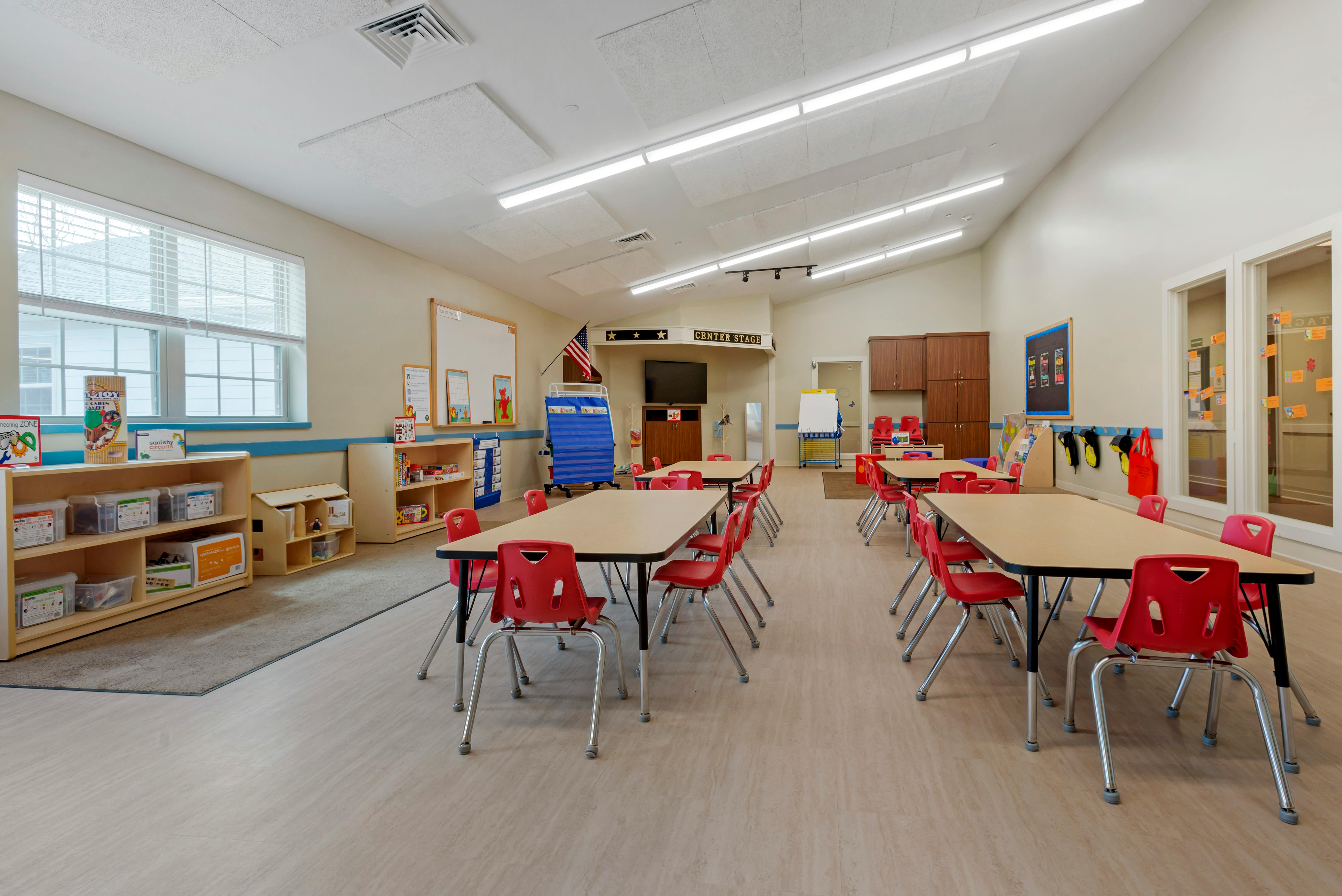 Classroom with child-sized tables and red chairs arranged in rows