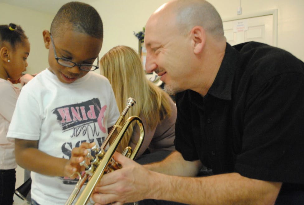 Adult helping a child play a trumpet