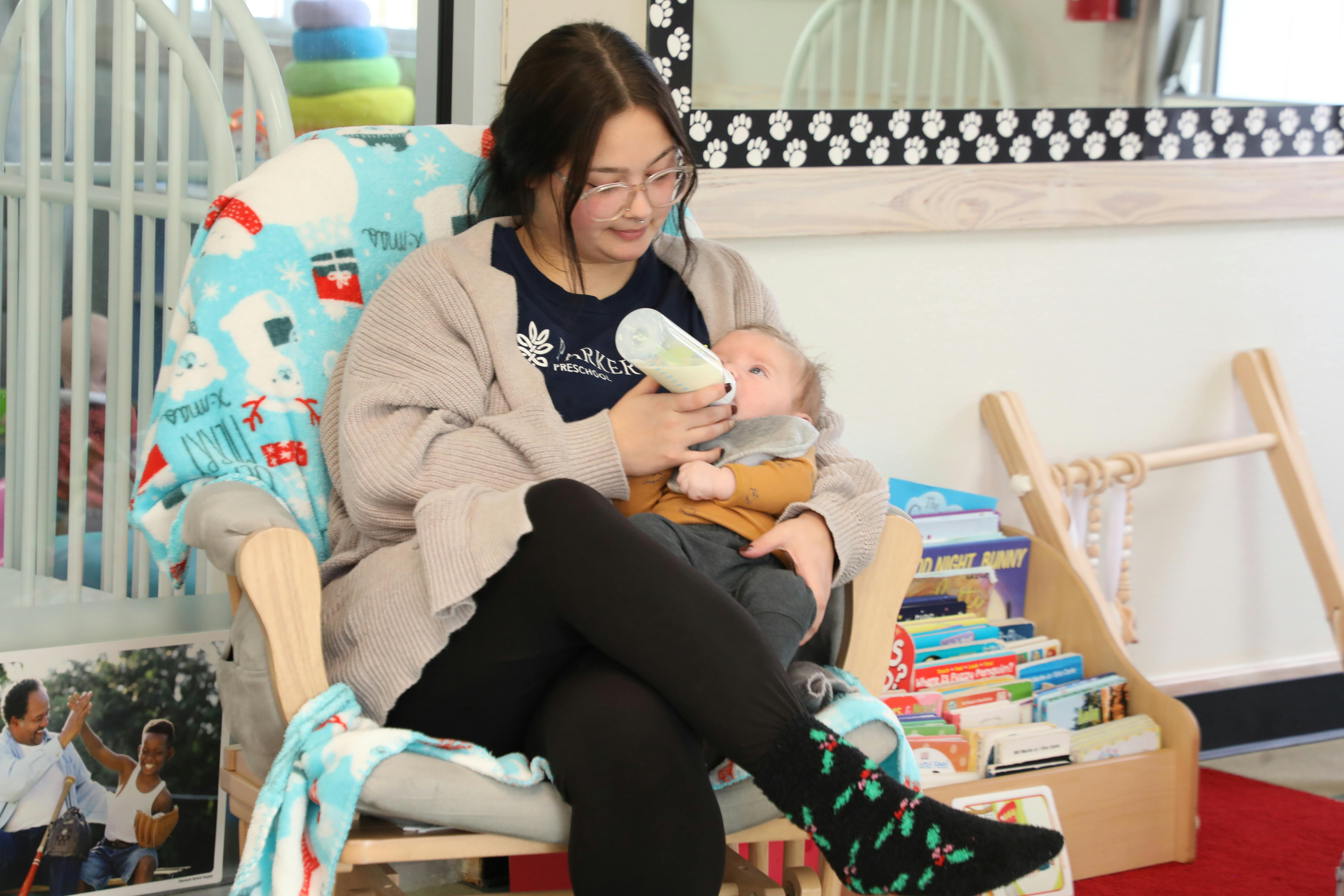 Person sitting in a chair feeding a baby a bottle