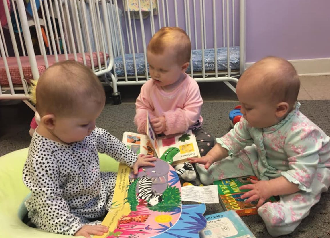 Three babies sitting on the floor looking at books and touching books