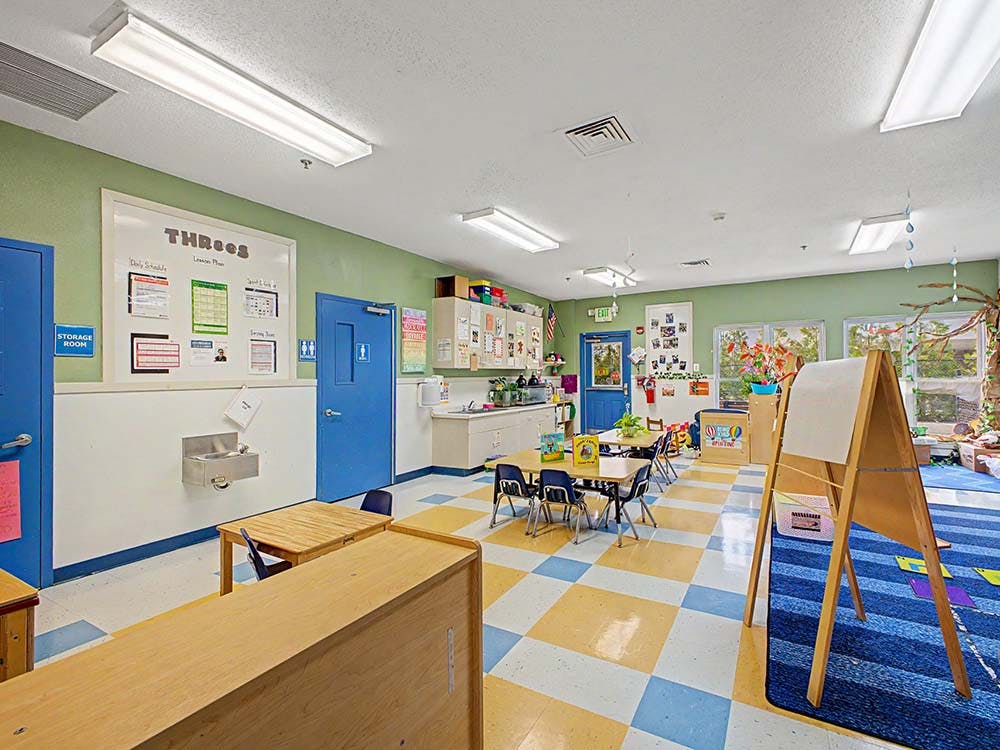 Classroom with child-sized tables and chairs, a sink, and a whiteboard