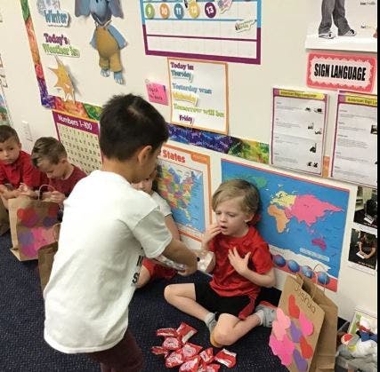 Child in white shirt giving something to child in red shirt in a classroom