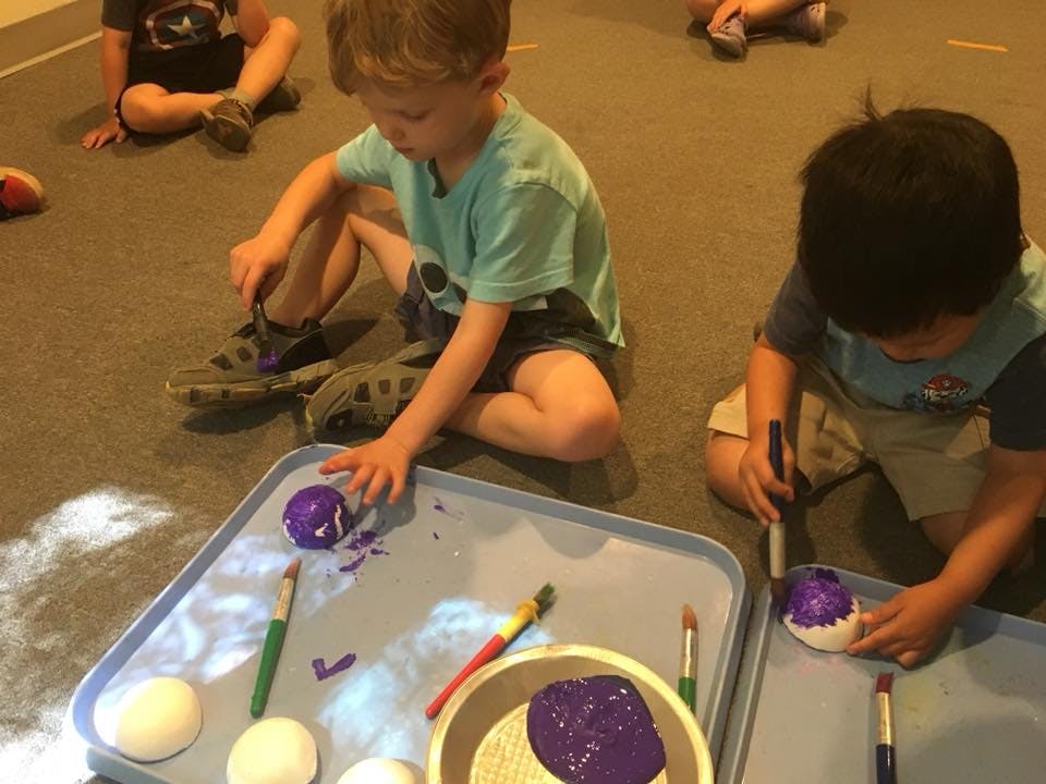 Two children painting objects on the floor