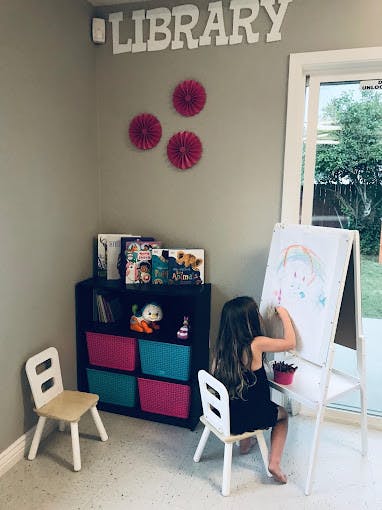 Child drawing on an easel in a room with a "LIBRARY" sign