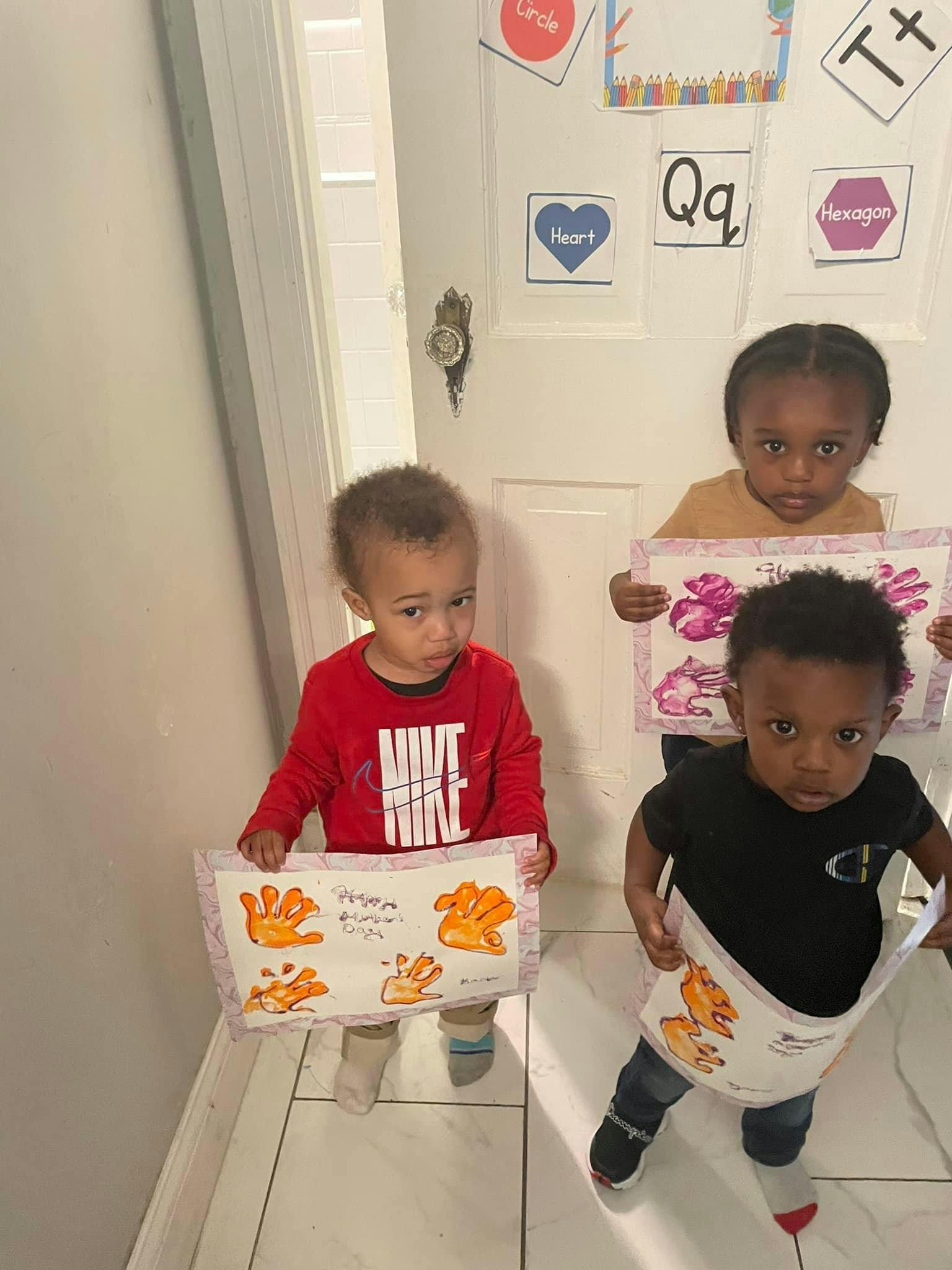 Three children holding up artwork with handprints