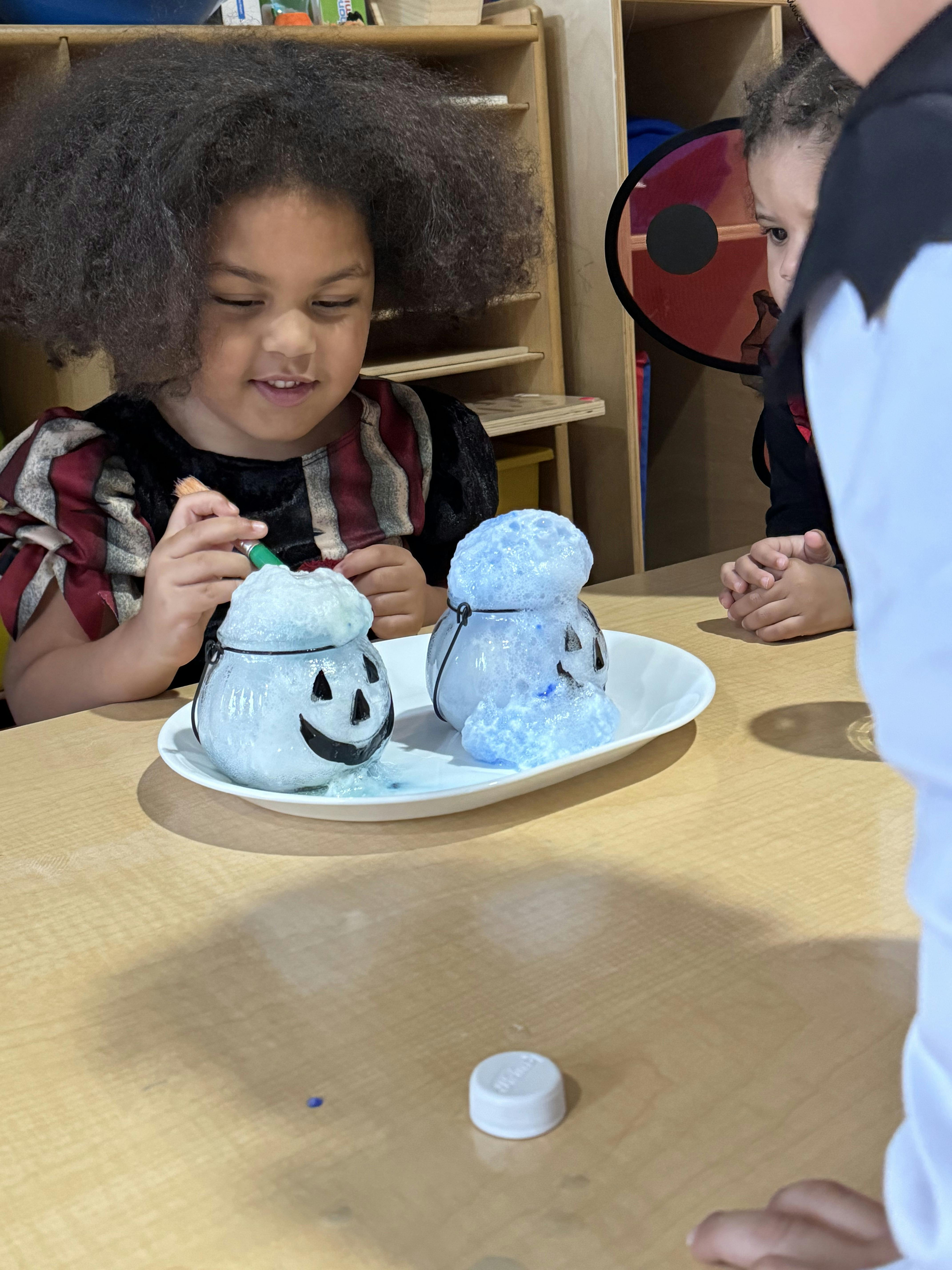 Child in costume painting a Halloween cauldron with bubbling blue liquid
