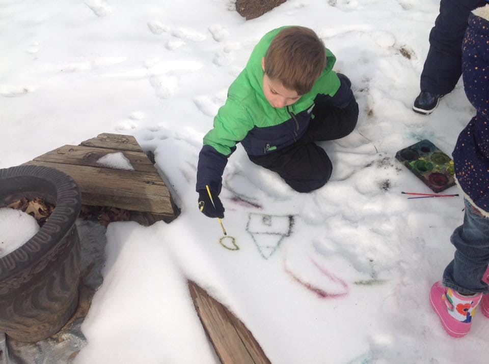 Child kneeling in snow, drawing with a stick