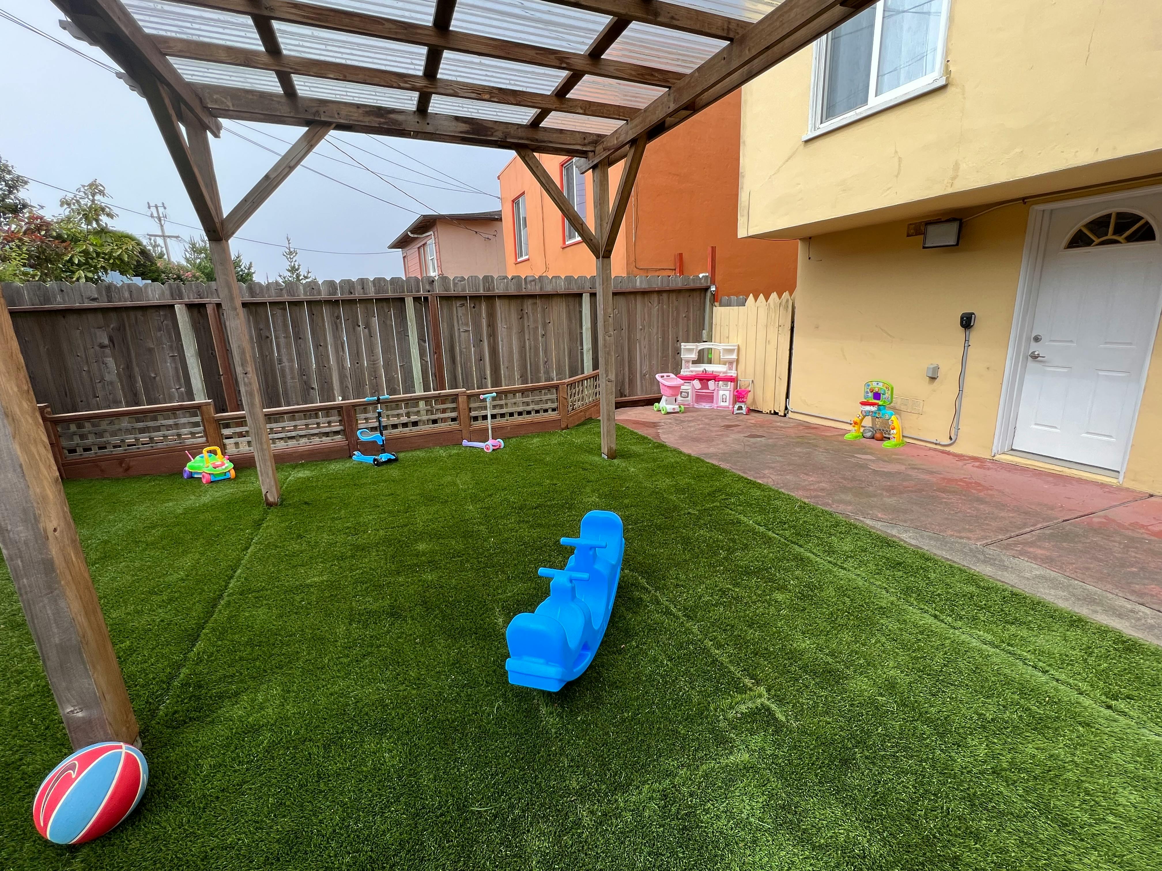 Backyard with artificial turf, a blue seesaw, and a wooden pergola