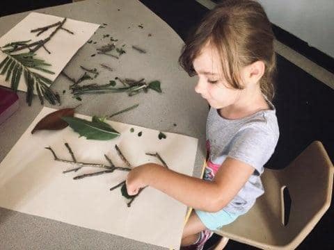 Child creating art with sticks and leaves on paper