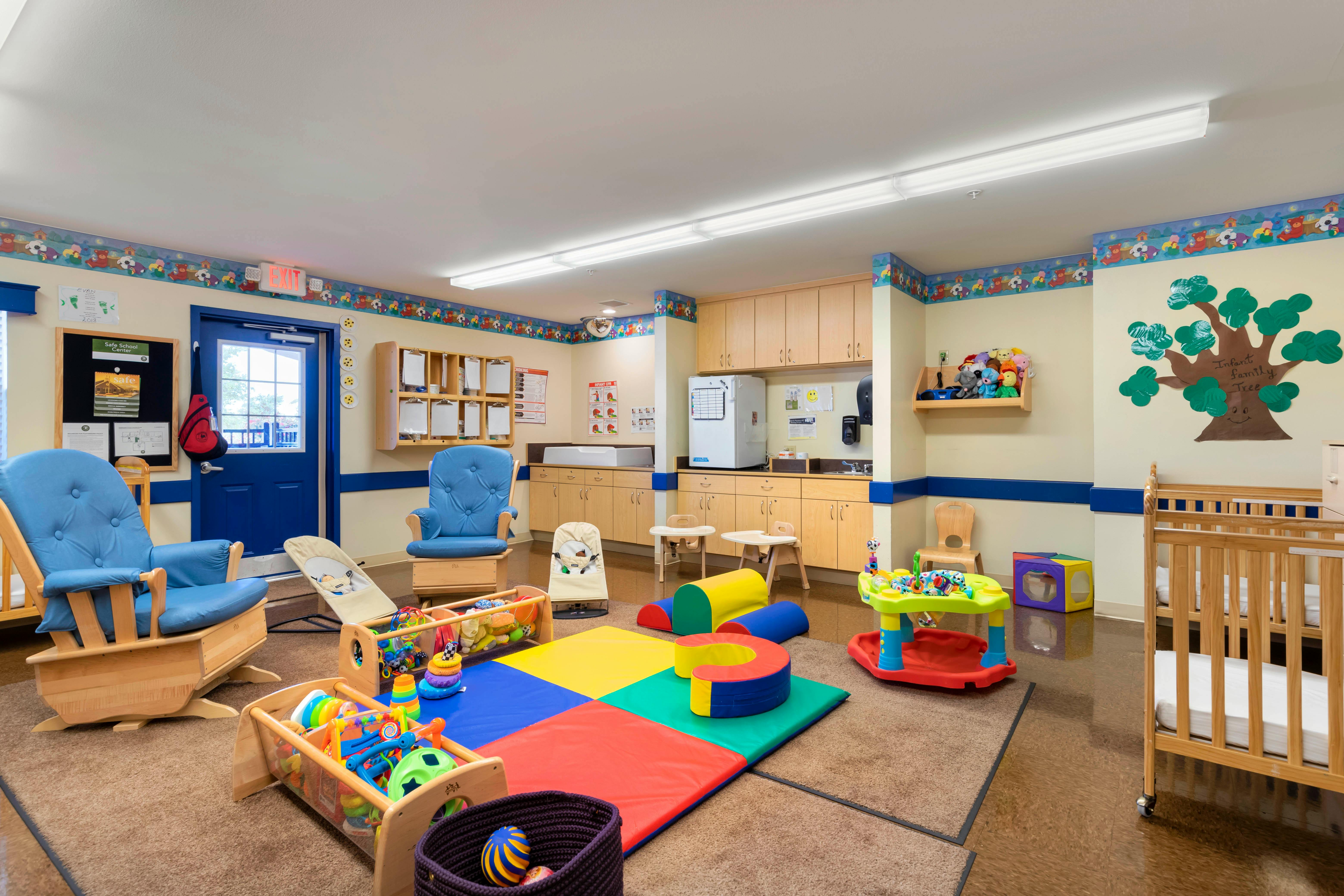An infant room with a rocking chair, cribs, changing table, and play area