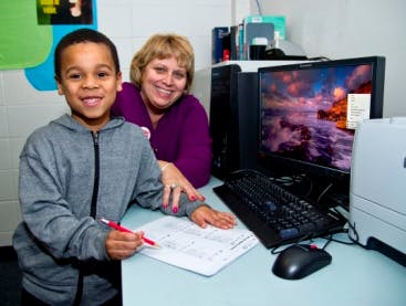 Child and adult at a computer, child holding a pen over paper