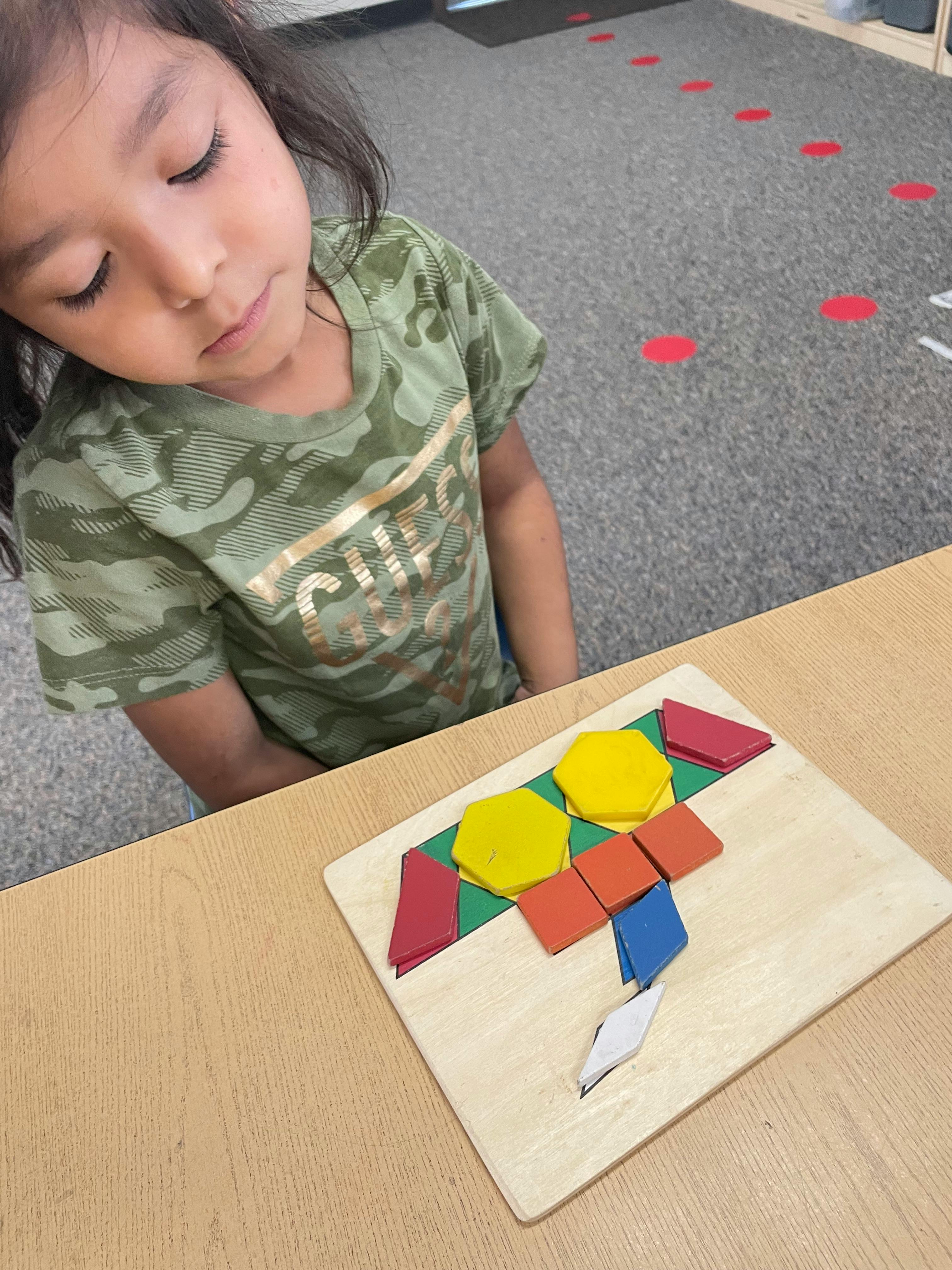 Child looking at a pattern block puzzle on a table